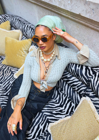Woman wearing a mint green metallic turban and sunglasses, seated on a zebra-print sofa