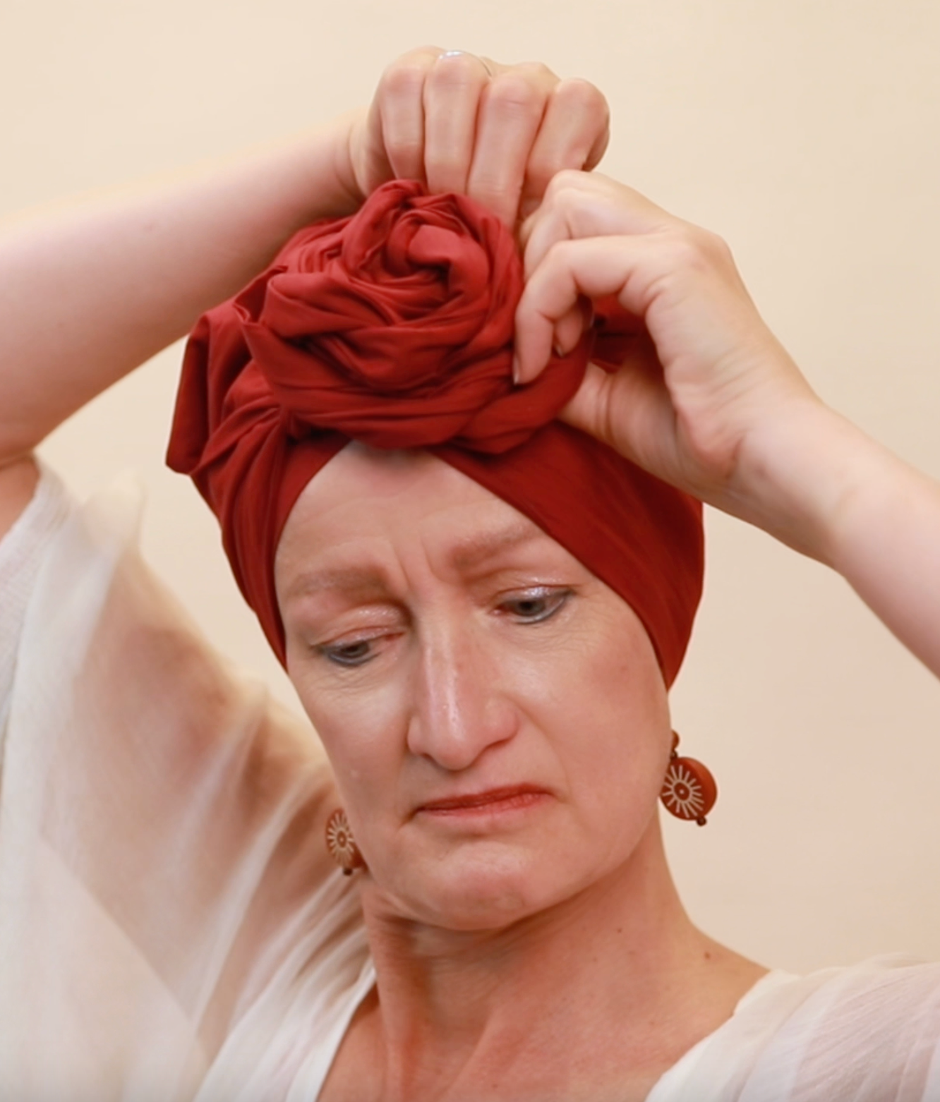 Woman tying her red, satin-lined turban with both hands into the Rose Crown style