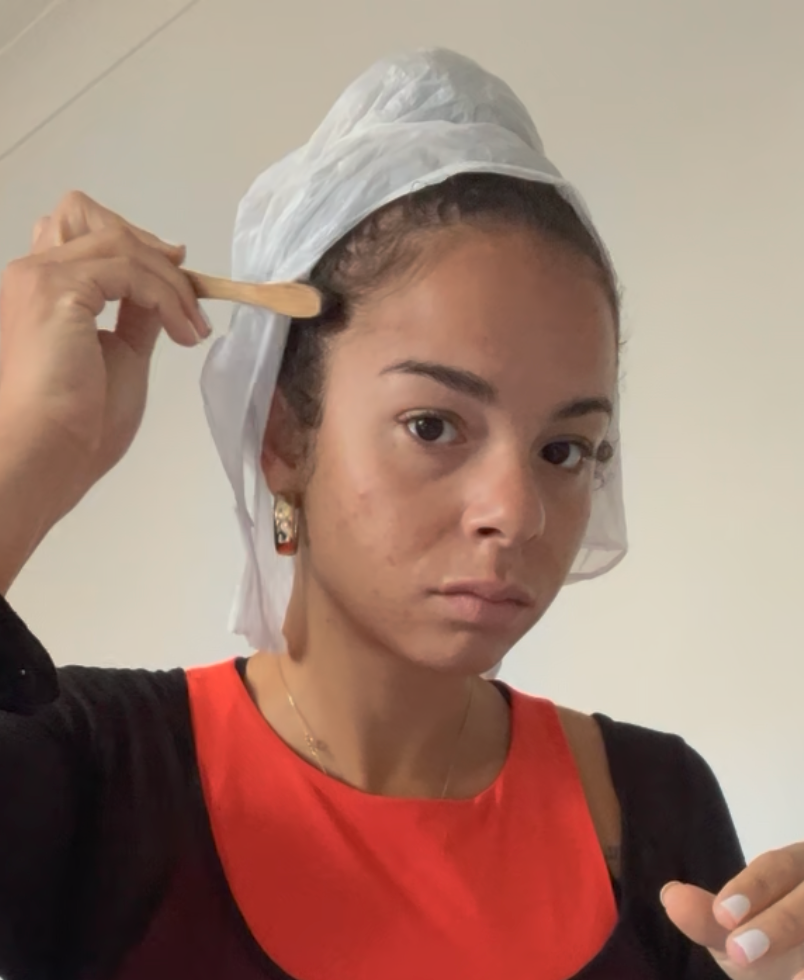 Woman using a hair edge brush to style her edges along her hairline, with a white plastic bag loosely draped over her hair, not yet secured