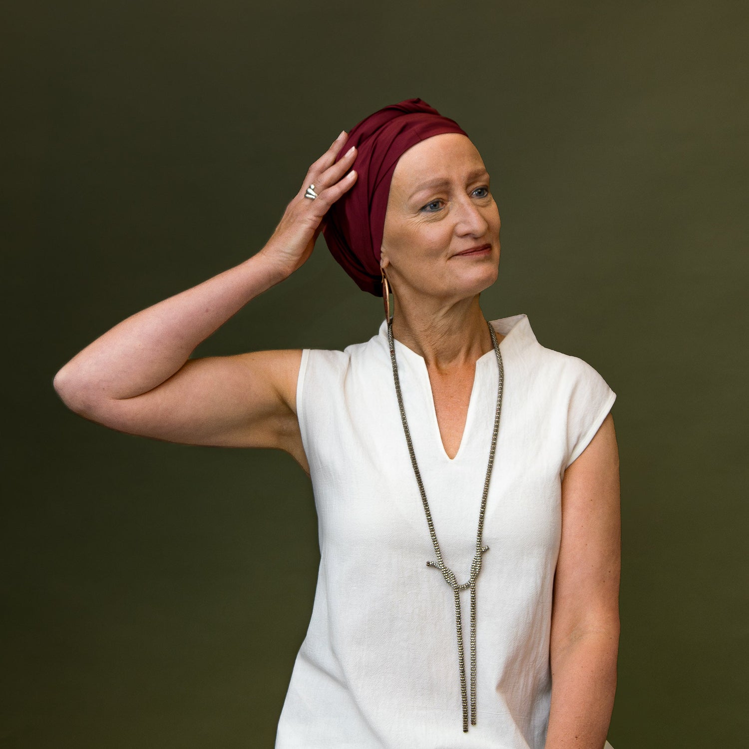 Woman wearing a red turban, a white shirt and a statement necklace, posed with her hand on her turban