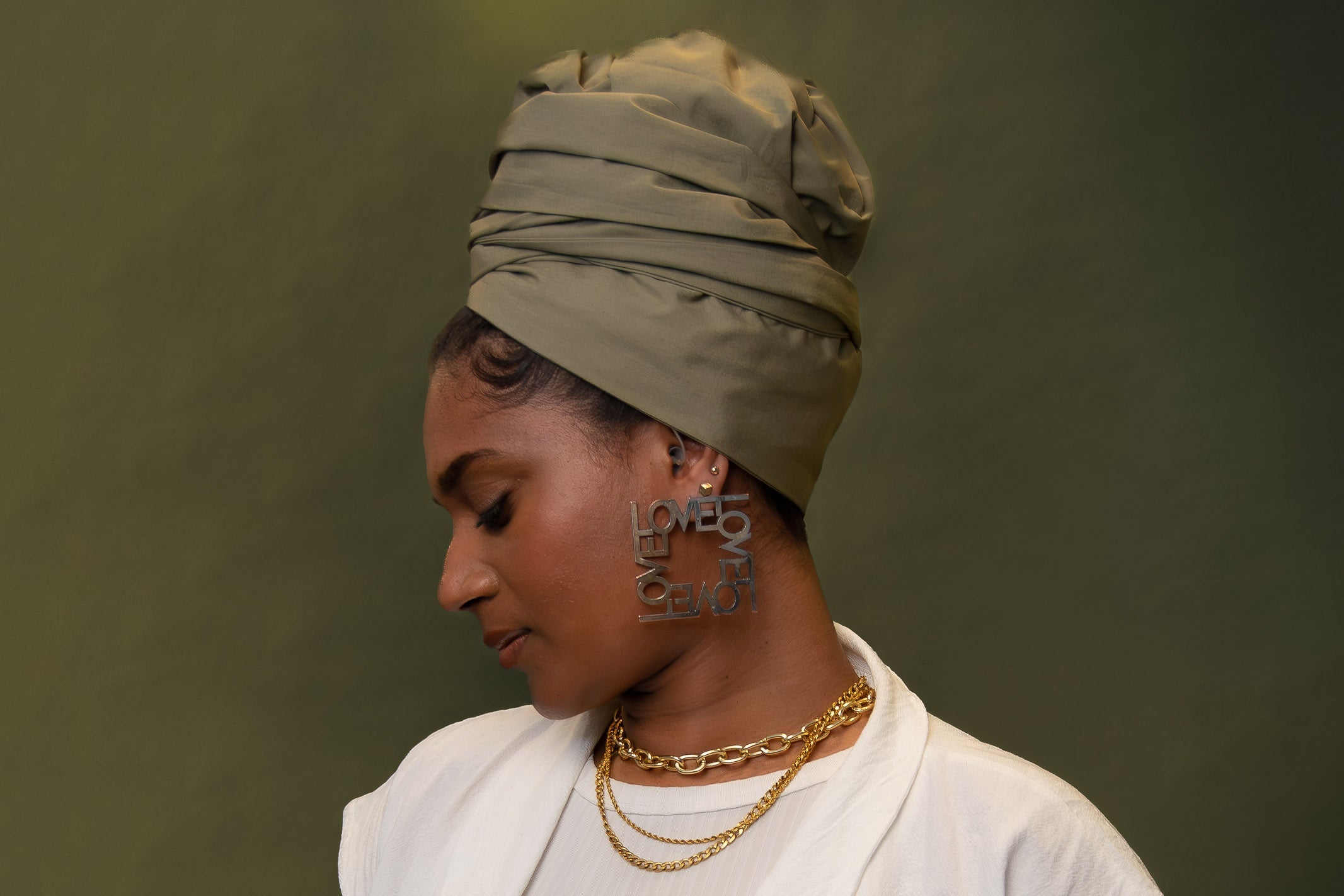 Woman wearing sage green satin-lined turban and earrings that spell out LOVE, green background
