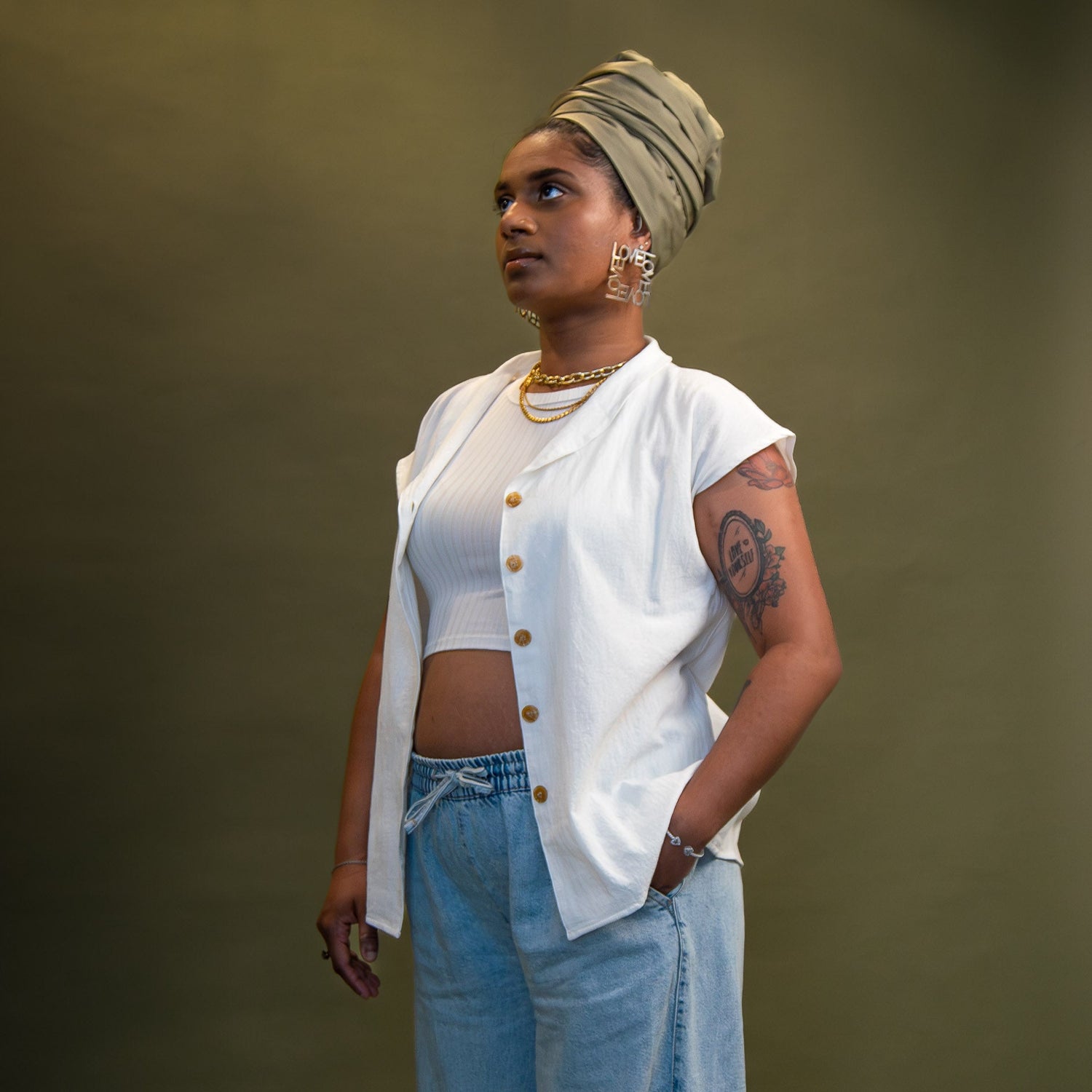Woman wearing a sage green satin-lined turban, white shirt, posed with her hand in her trouser pocket