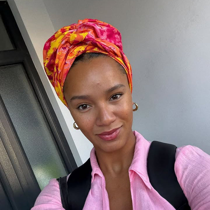 Woman wearing an orange, yellow and pink patterned turban, smiling