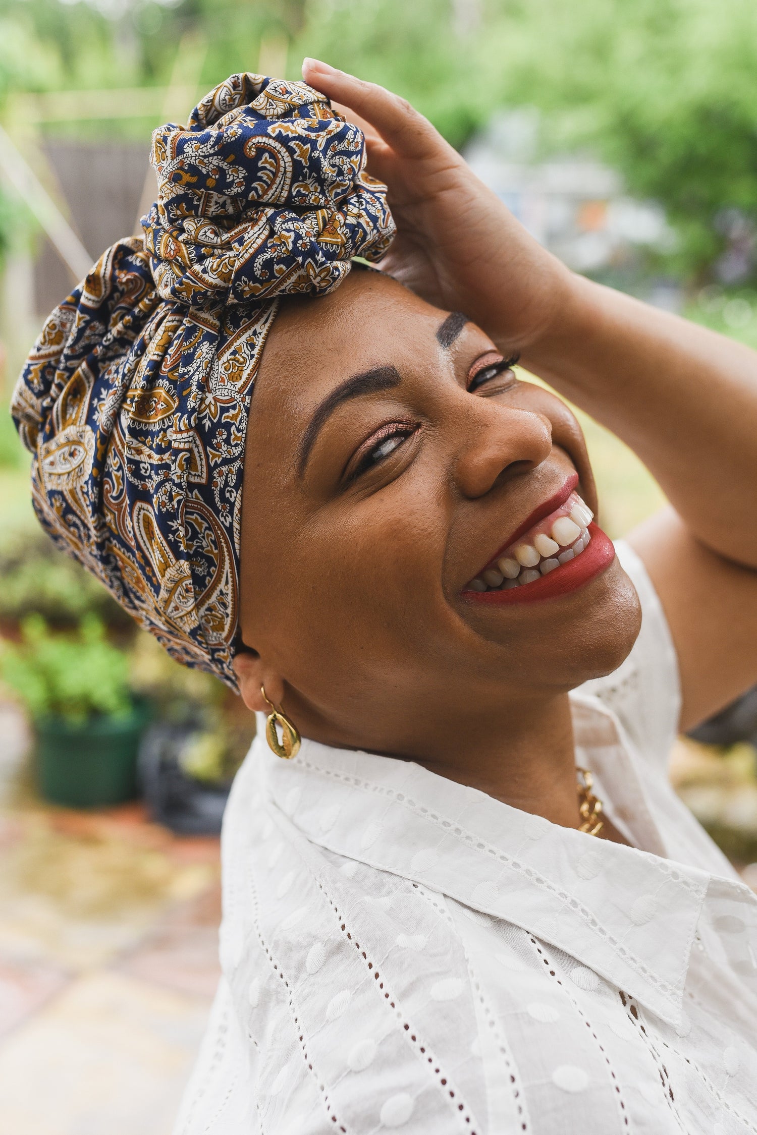 Woman wearing a patterned turban wrapped in the Rose Crown style, smiling at the camera