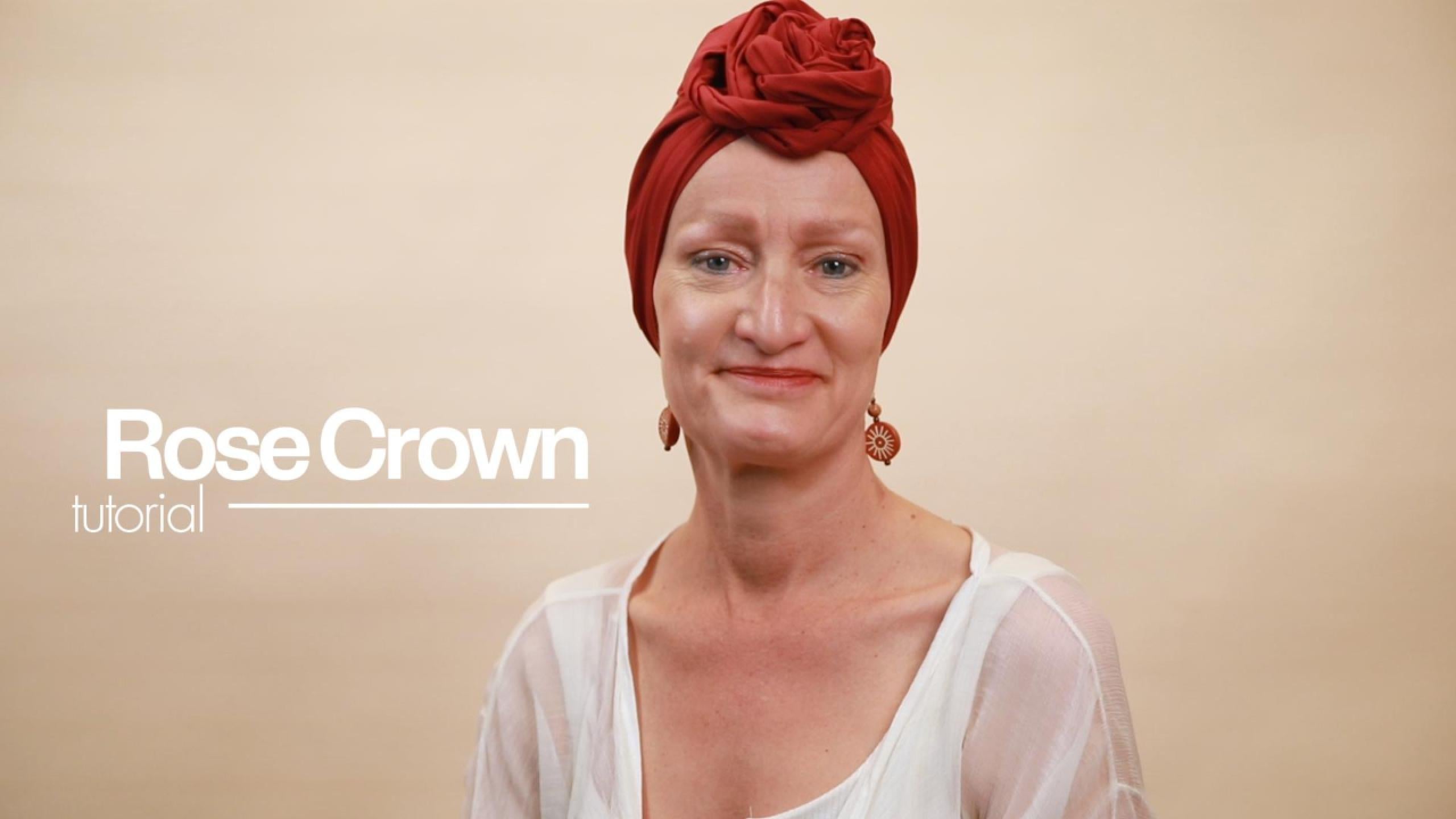 Load video: Rose Crown Tutorial - a woman with alopecia demonstrates how to wrap a satin-lined red turban into a Rose Crown style
